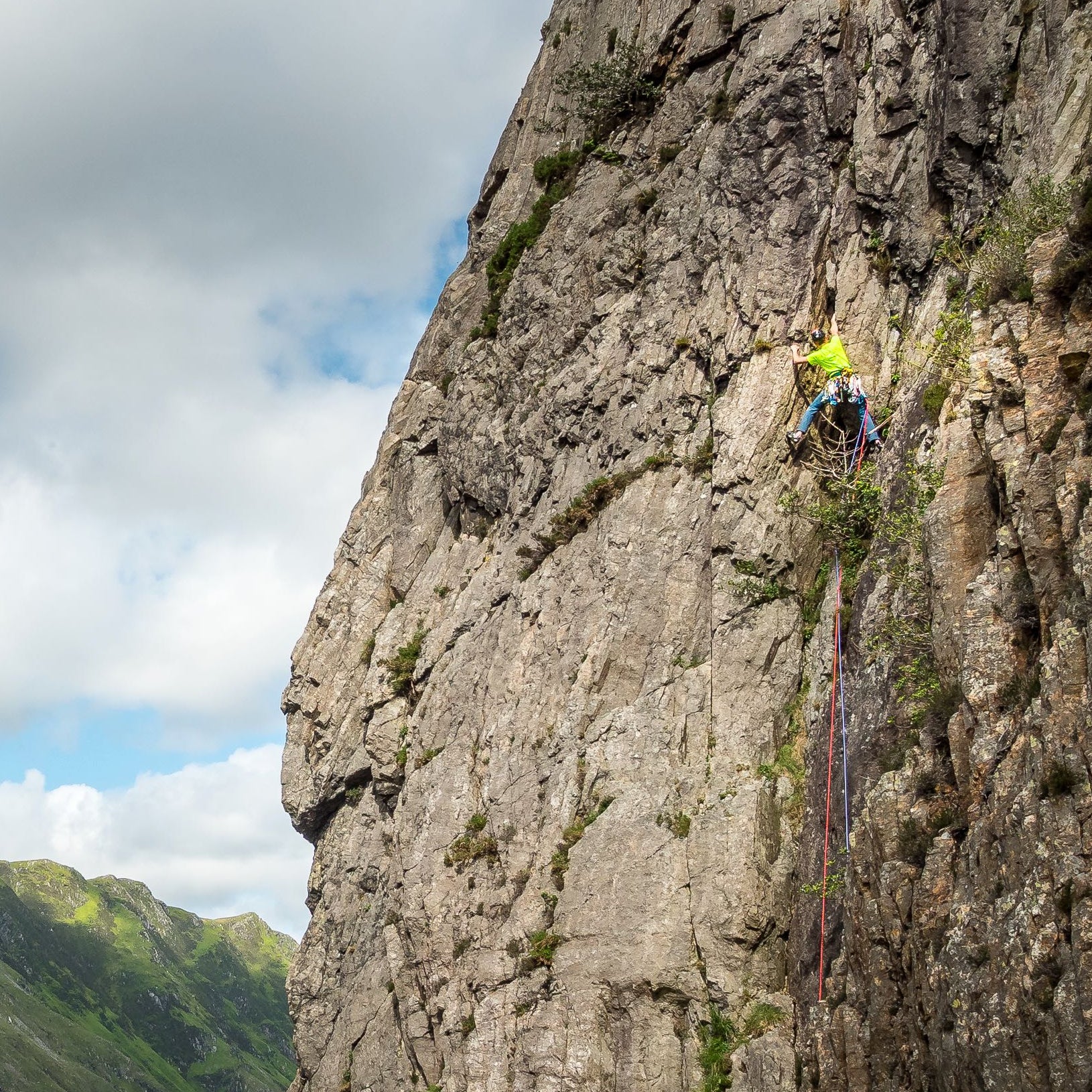 Person climbing a steep cliff face with mountains in the background