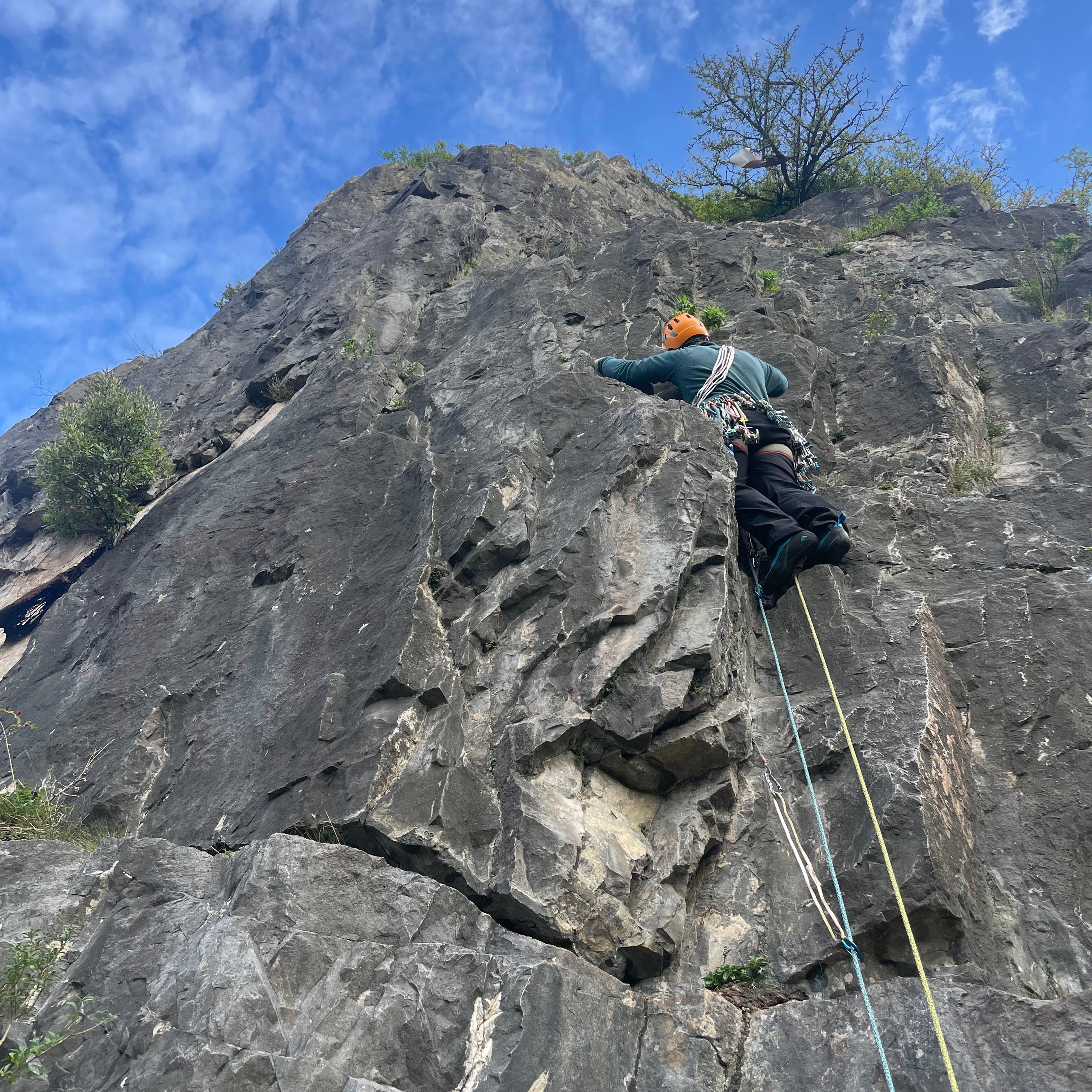 Person climbing a rocky cliff face with a clear blue sky in the background